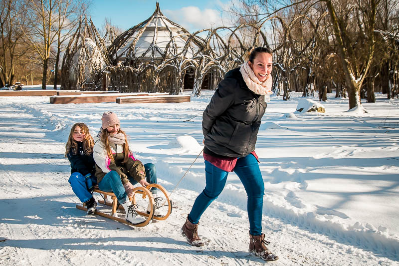 Mama zieht ihre Kinder auf dem Schlitten durch den Schnee beim Fotoshooting in Rostock.