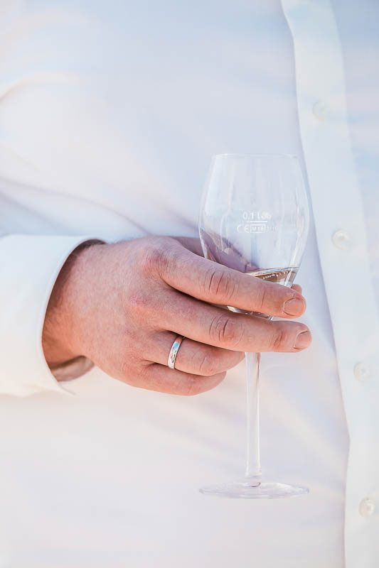 Sektglas in der Hand vom Bräutigam mit dem neuen Ehering