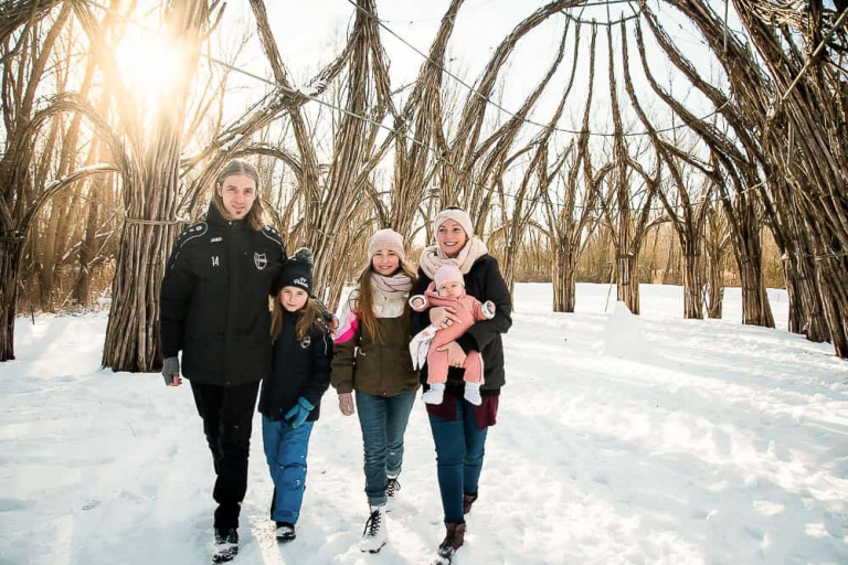 Familie läuft unter einem Weidendom entlang bei Sonnenschein und Winterlandschaft