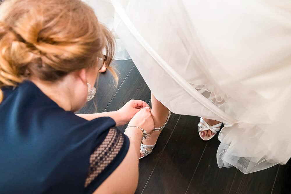 Getting Ready bei der Hochzeit. Die Trauzeugin hilft beim Anziehen der Schuhe für die Braut.