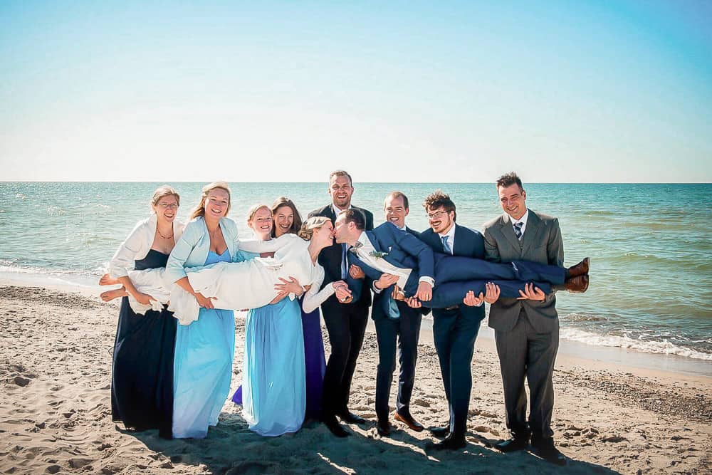 Braut und Bräutigam werden von ihren Freunden und Freundinnen am Strand getragen.