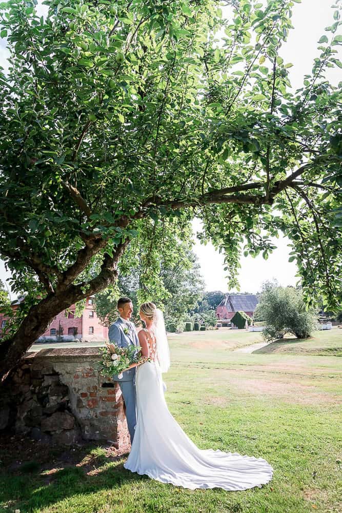 Hochzeitslocation Gut Gerdshagen dient als perfekte Kulisse für die Hochzeitsfotos. Das Brautpaar steht unter einem Baum und schaut sich an. Hochzeitsfotograf in Satow.