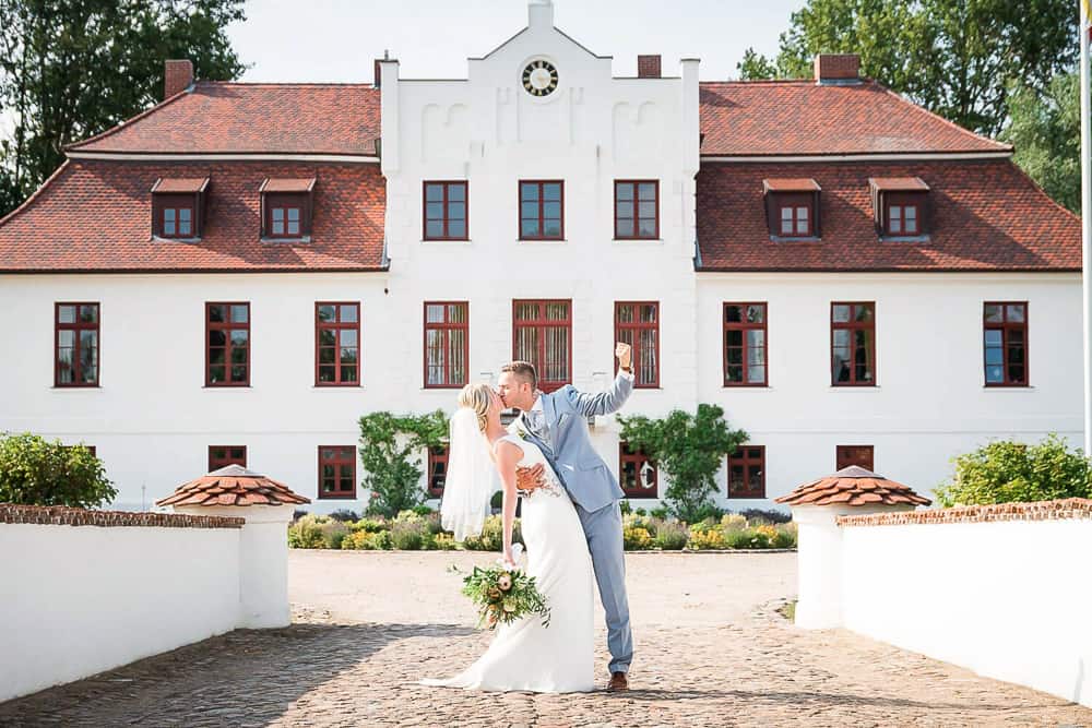 Brautpaar jubelt vor dem Gutshaus Gerdshagen nach der emotionalen freien Trauung. Eine wunderschöne Hochzeitslocation in der Nähe von Rostock. Hochzeitsfotograf Satow.
