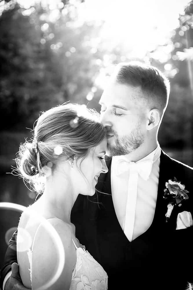 Bräutigam gibt seiner Braut einen Kuss auf die Stirn. Schwarzweiß-Foto mit Light Leaks. Hochzeitsfotograf Rostock.