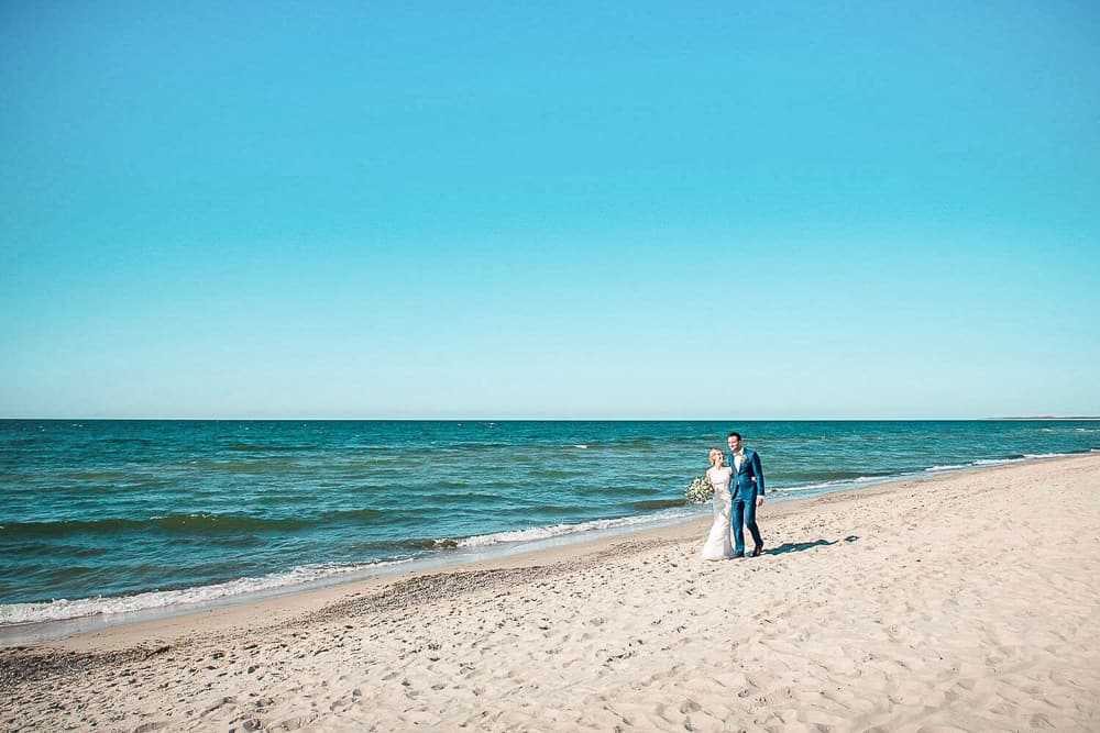 Hochzeitsfotos am Strand von Dierhagen auf dem Darß. Das Brautpaar spaziert am weißen Sandstrand entlang.