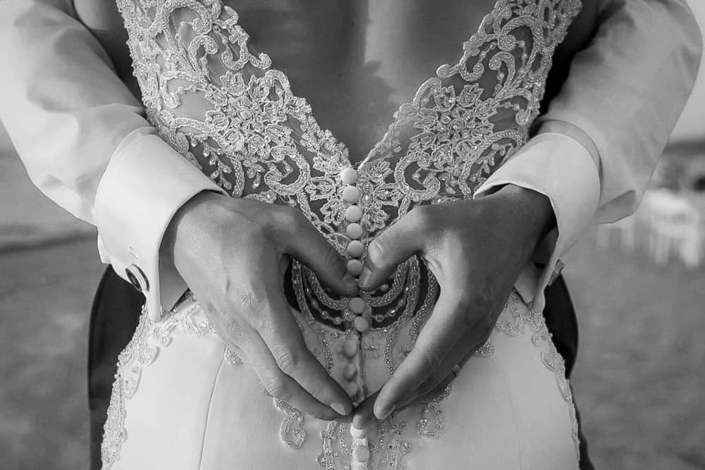 Schwarzweißfoto von einer Detailaufnahme: Hochzeitskleid und ein Herz geformt aus den Händen des Ehemannes. Hochzeitsfotograf Darß.