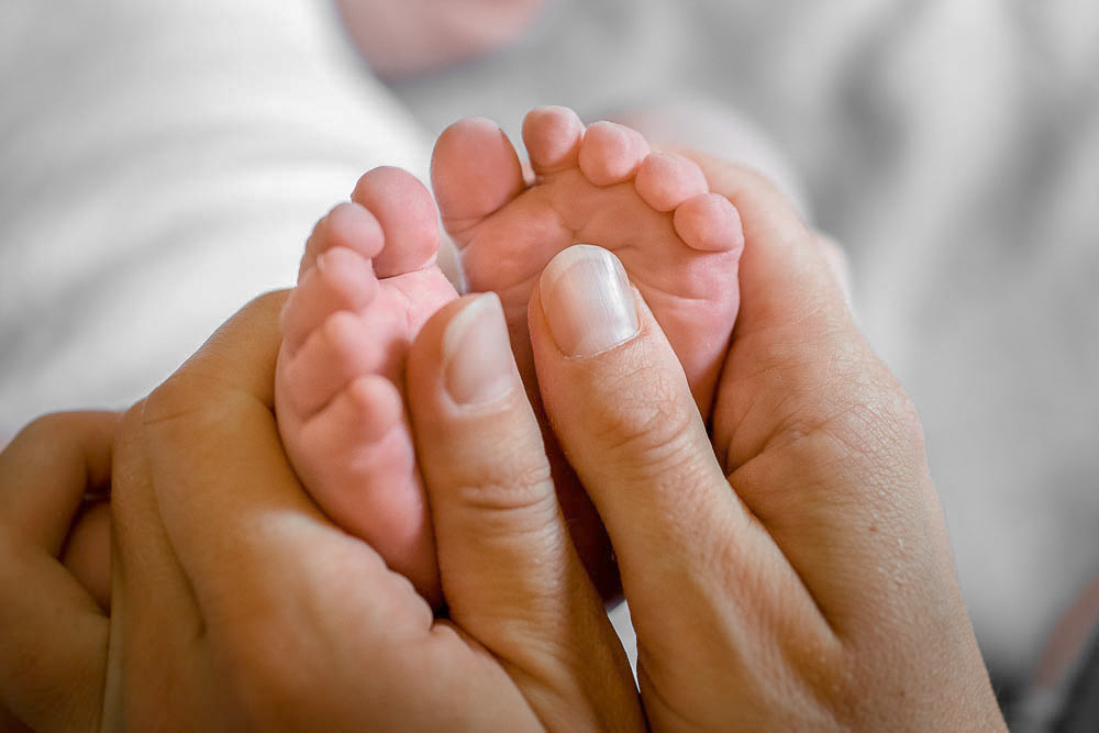 Mama hält die Füße ihres neugeborenen Babys in der Hand