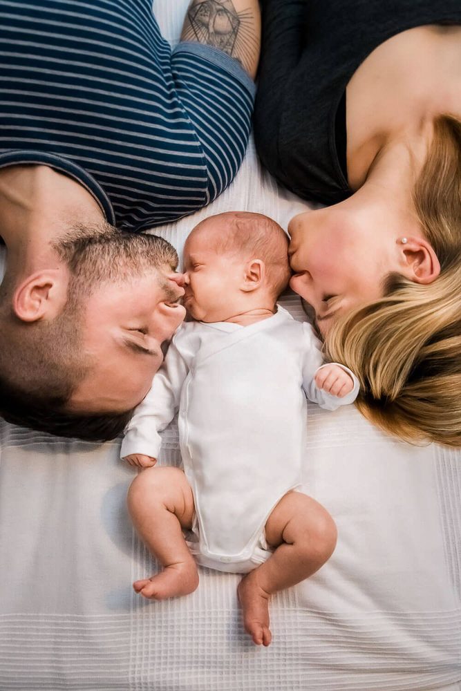 Eltern liegen im Bett und geben ihrem neugeborenen Baby einen Kuss.
