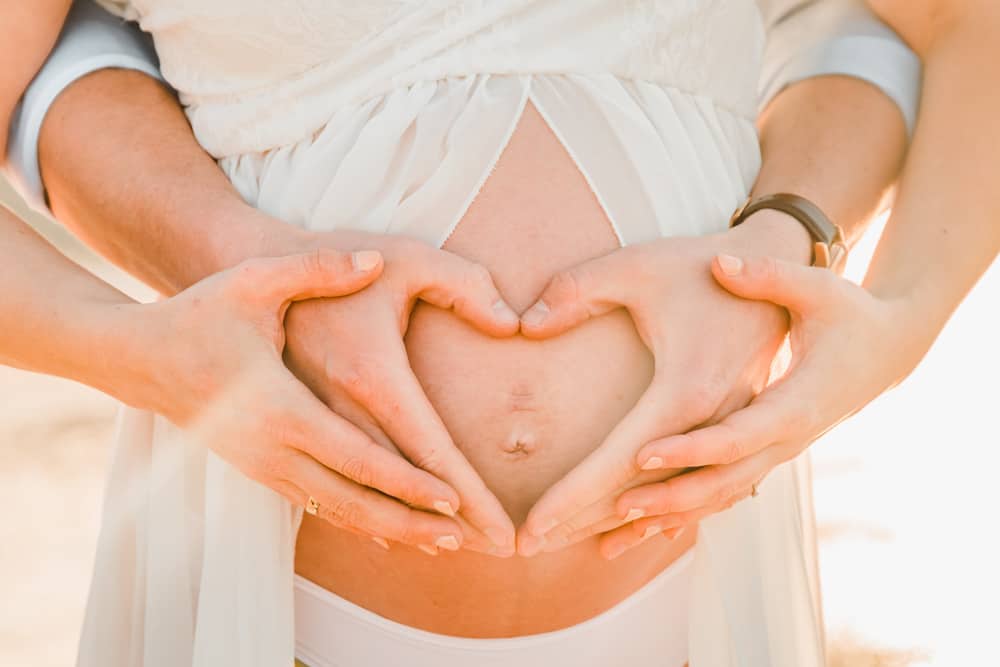 Mann und Frau formen ein Herz auf dem Babybauch.