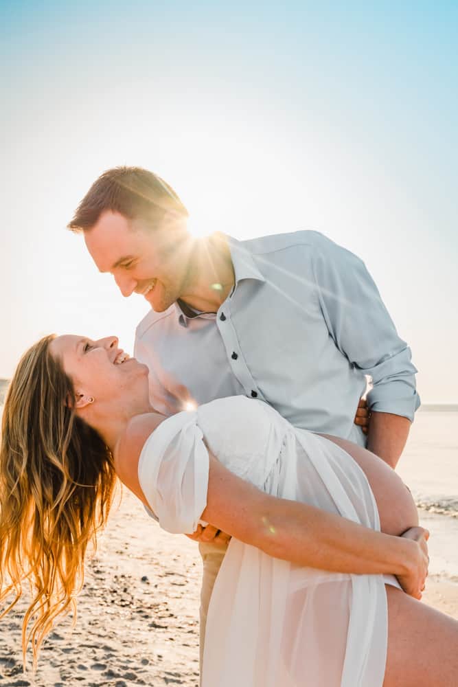 Mann tanzt mit seiner schwangeren Frau am Strand.