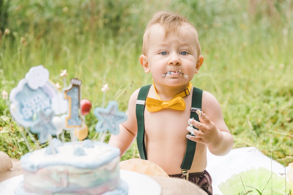 Kleinkind isst seinen Geburtstagskuchen auf einer Wiese