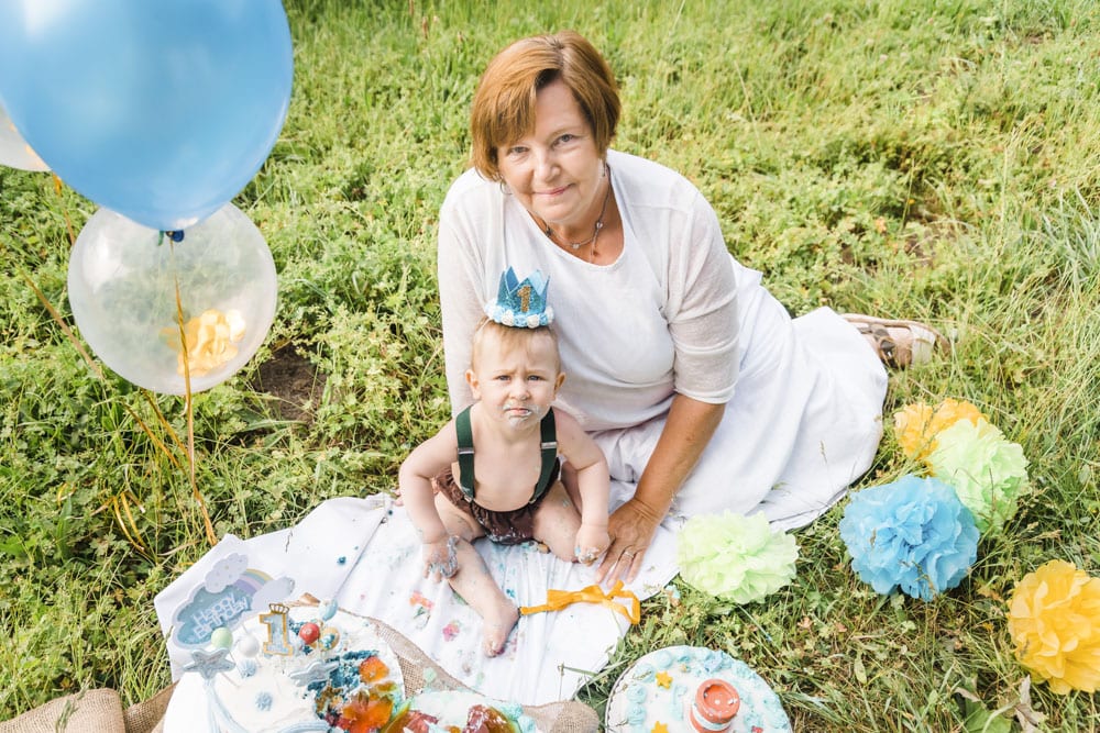 Oma sitzt mit ihrem Enkel zum ersten Geburtstag auf einer Wiese