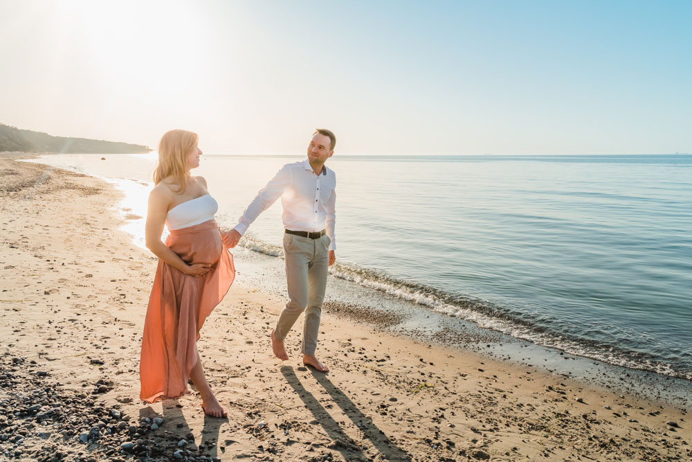 Schwangere Frau und werdender Papa laufen am Ostsee-Strand entlang.