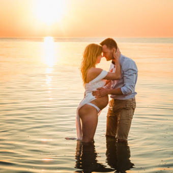 Schwangere Frau und ihr Mann stehen zum Sonnenuntergang im Wasser