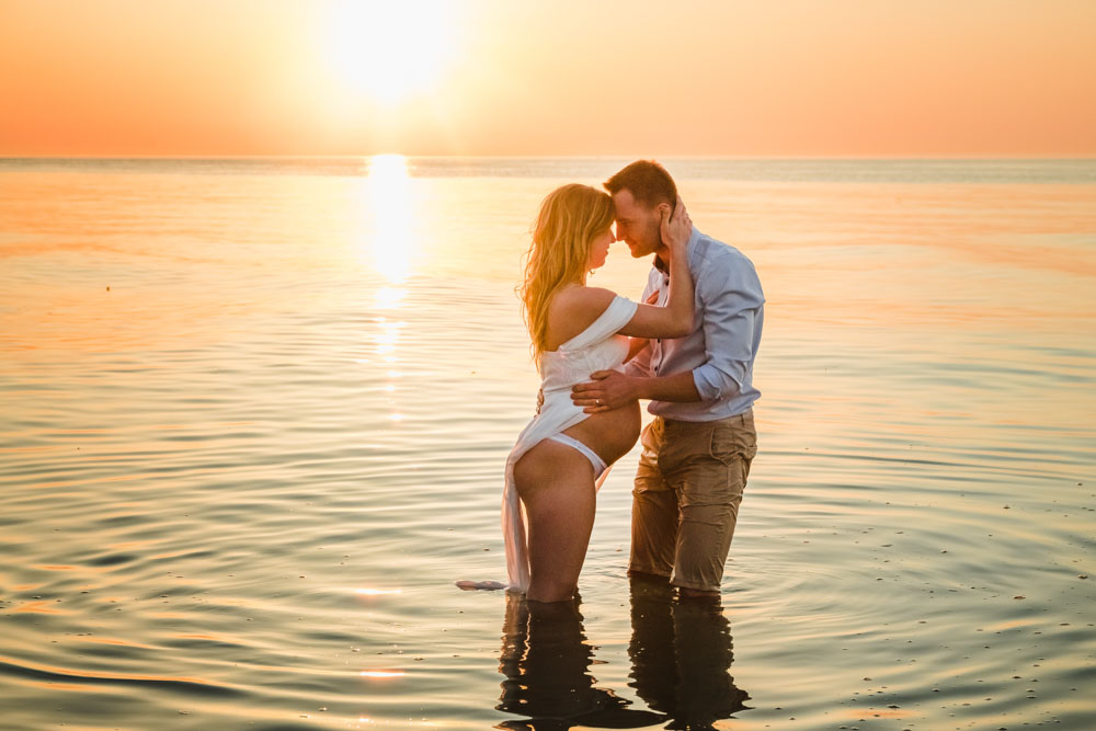 Schwangere Frau und ihr Mann stehen zum Sonnenuntergang im Wasser