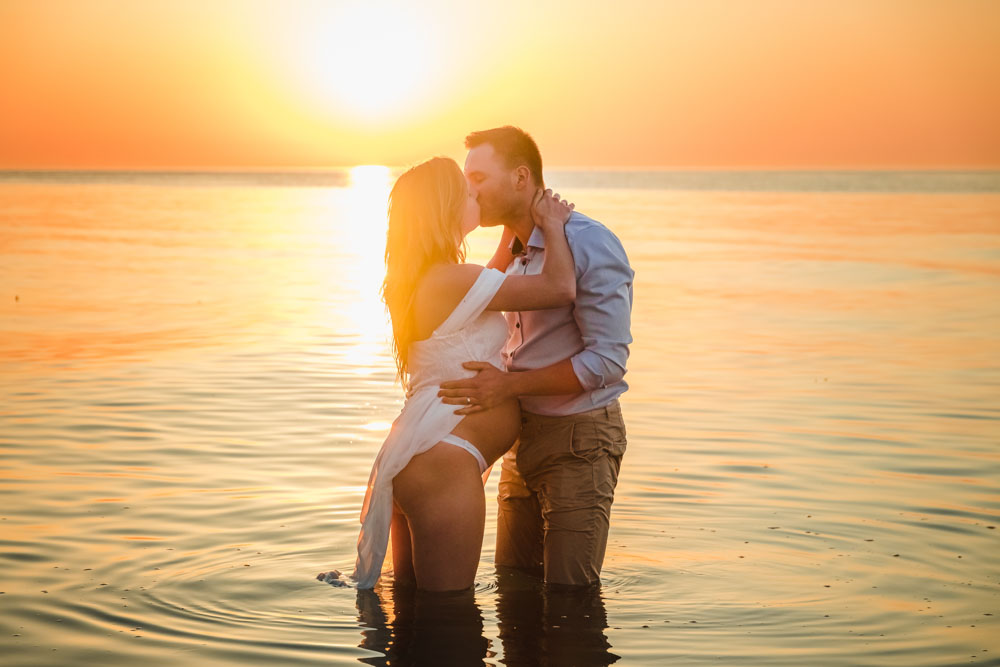 Schwangere Frau und Mann küssen sich während des Sonnenuntergangs im Wasser