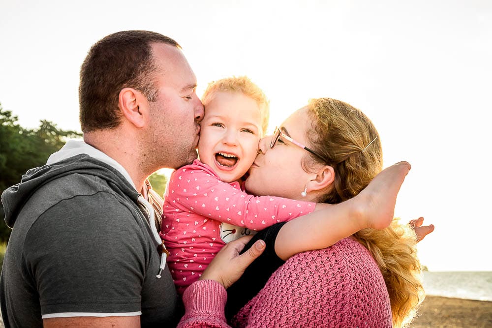 Mama und Papa geben ihrer Tochter einen Kuss auf die Wange