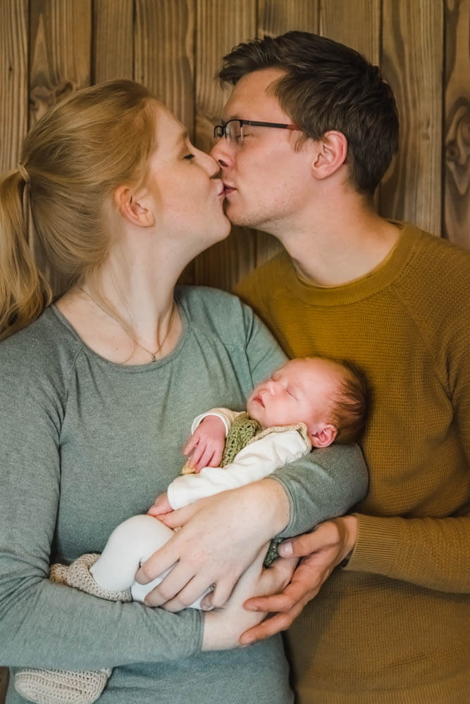 Eltern halten ihr neugeborenes Baby im Arm und küssen sich.