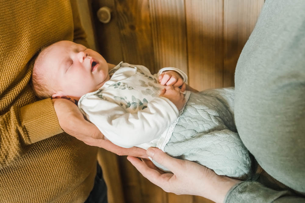 Neugeborenes Baby wird zwischen frischgebackenen Eltern gehalten. Babyfotograf Rostock.