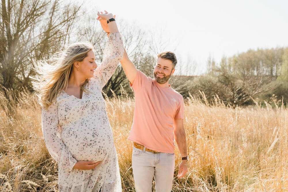 Schwangere und ihr Mann tanzen beim Babybauchfotoshooting in Rostock auf einem vertrocknetem Feld