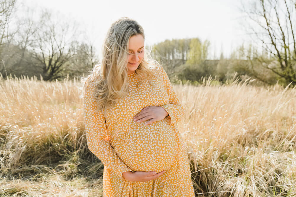 Schwangere erwartet Zwillinge und steht auf einem vertrocknetem Feld in einem gelben Kleid