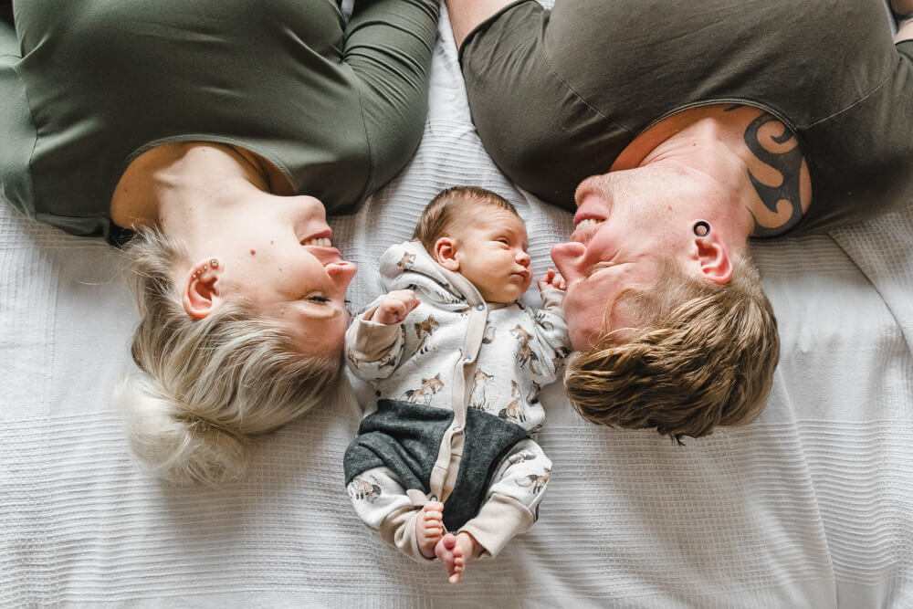 Neugeborenes Baby liegt zwischen Mama und Papa beim Babyfotoshooting Zuhause im Bett
