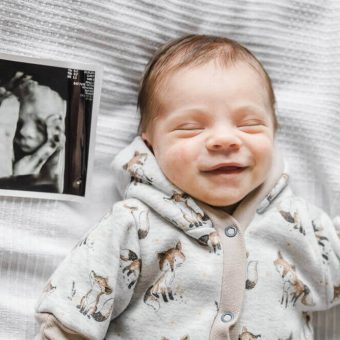 Baby lacht beim Schlafen und neben ihm liegt ein 3D-Ultraschallbild aus der Schwangerschaft