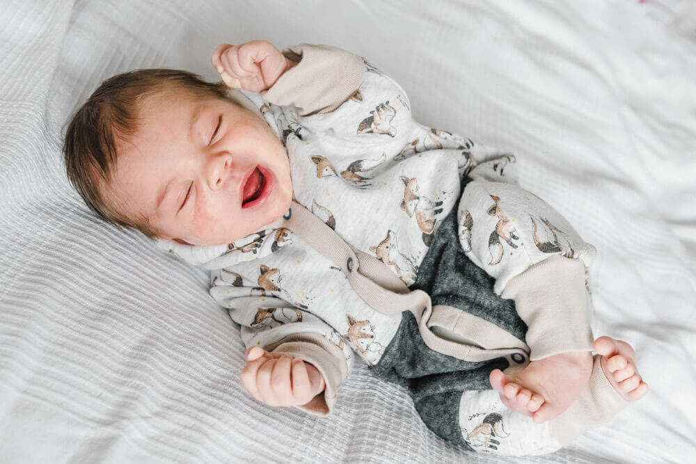 Lachendes Baby beim Schlafen beim Babyfotoshooting Zuhause auf weißer Decke