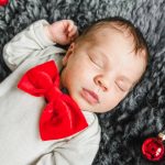 Baby beim Babyfotoshooting Zuhause mit roten Weihnachtskugeln und roter Schleife. Babyfotograf Rostock.