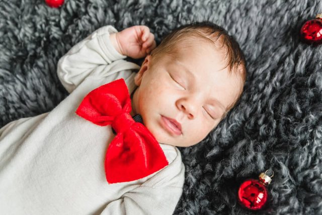 Baby beim Babyfotoshooting Zuhause mit roten Weihnachtskugeln und roter Schleife. Babyfotograf Rostock.