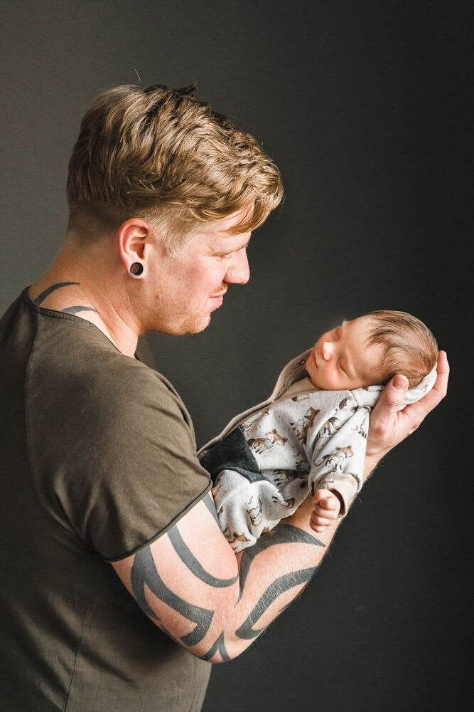 Papa hält sein neugeborenes Baby auf dem Arm im Profil beim Babyfotoshooting Zuhause