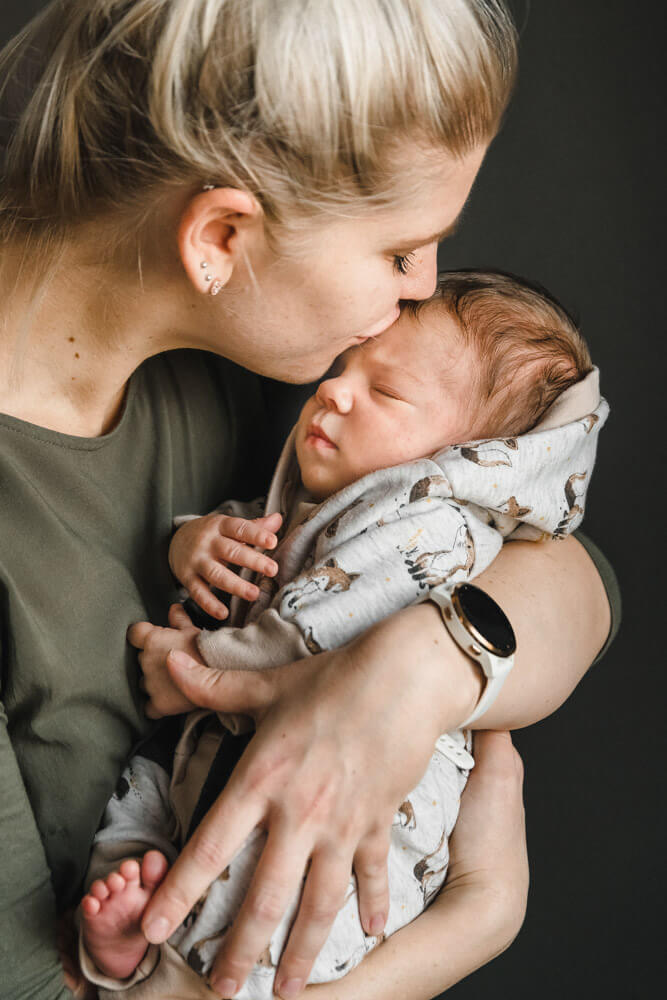 Mama gibt ihrem neugeborenen Baby einen Kuss auf die Stirn beim Babyfotoshooting Zuhause