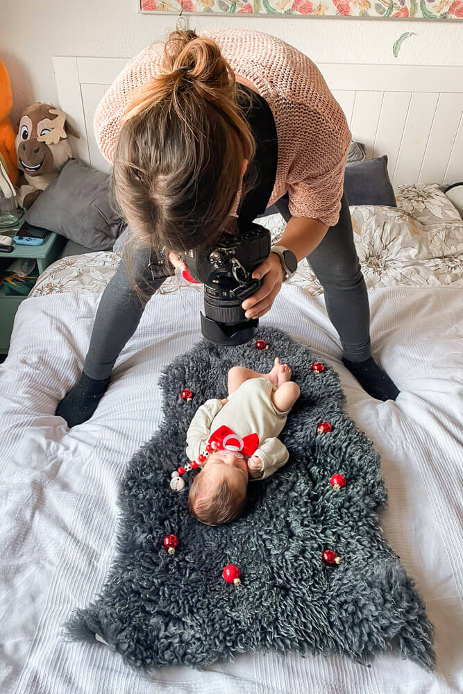 Fotografin fotografiert neugeborenes Baby mit Weihnachtsoutfit Zuhause beim Fotoshooting