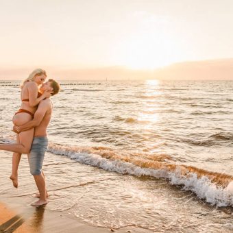 Mann hebt seine Freundin am Strand zur goldenen Stunde hoch