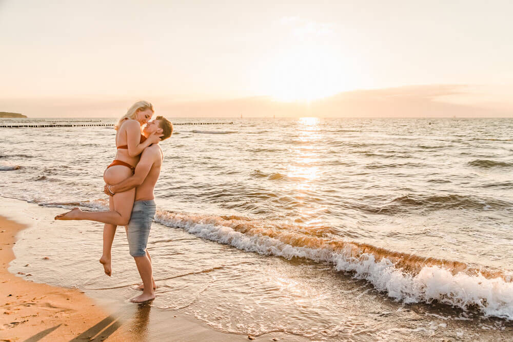 Mann hebt seine Freundin am Strand zur goldenen Stunde hoch
