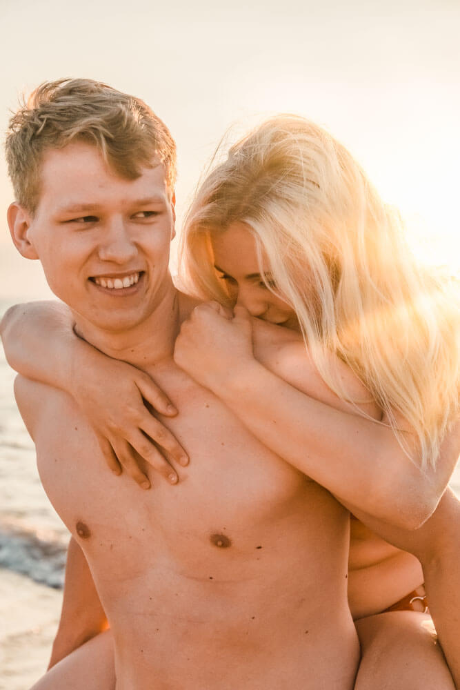 Frau küsst Schulter von Mann beim Pärchenshooting am Strand zur goldenen Stunde