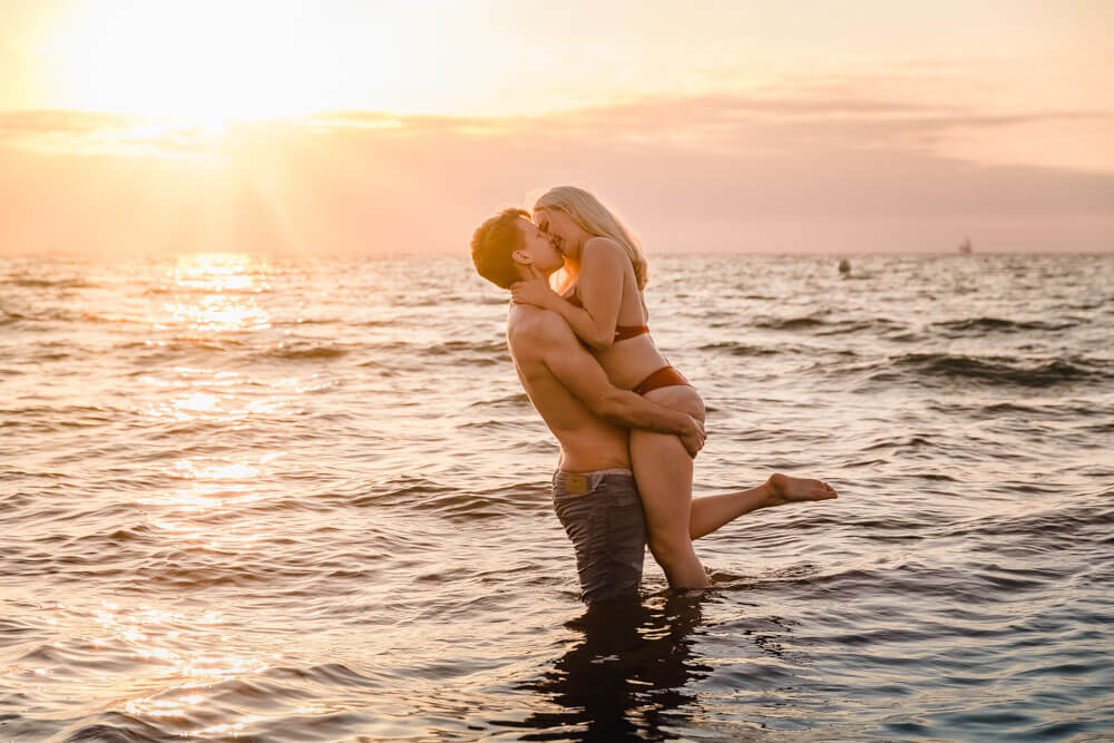 Paarfoto am Strand in der Ostsee zum Sonnenuntergang. Die Frau wird hochgehoben.