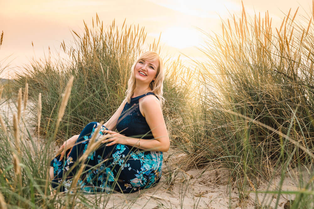 Blonde junge Frau sitzt in den Dünen am Strand von Warnemünde zur goldenen Stunde