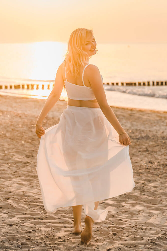 Blonde junge Frau mit weißem Rock läuft am Strand von Warnemünde zur Sonne