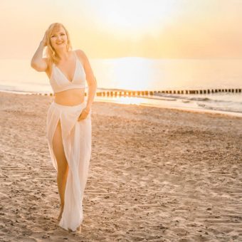 Junge blonde Frau trägt weiße Kleidung zum Sonnenuntergang am Strand von Warnemünde
