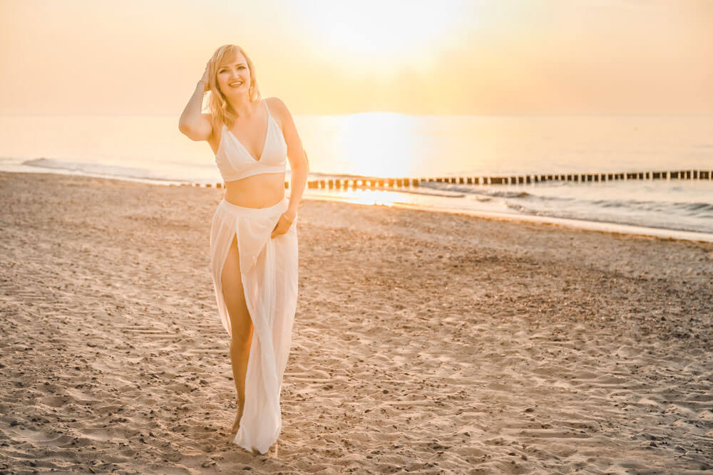 Junge blonde Frau trägt weiße Kleidung zum Sonnenuntergang am Strand von Warnemünde
