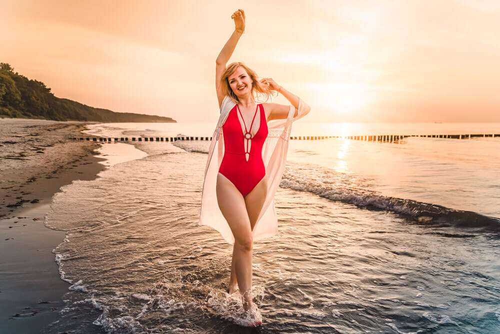 Junge Frau trägt beim Fotoshooting in Warnemünde einen roten Bikini und läuft durch das Wasser.