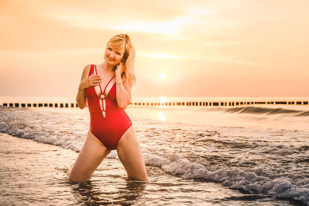 Junge Frau posiert sexy in einem roten Badeanzug beim Sonnenuntergang in der Ostsee in Warnemünde.