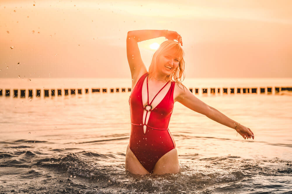 Junge Frau beim Sonnenuntergang in der Ostsee mit einem roten Badeanzug.