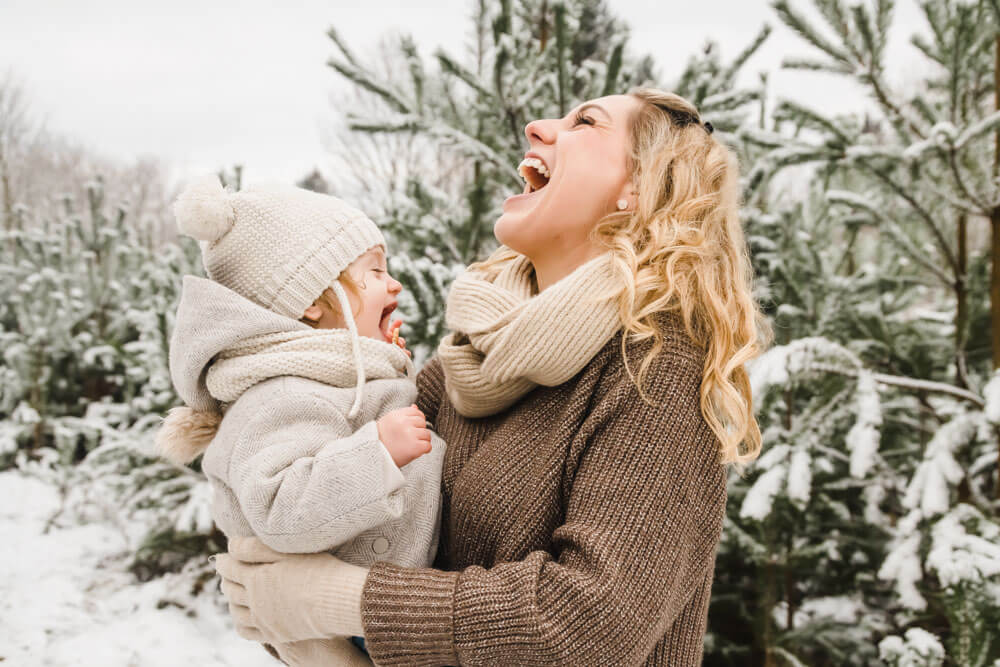 Kleinkind und Mama lachen herzhaft bei Familienfotos im Schnee in HRO