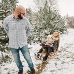 Papa zieht Tochter, Mama und Hündin auf einem Schlitten durch den Schnee im Winter beim Fotoshooting in Rostock