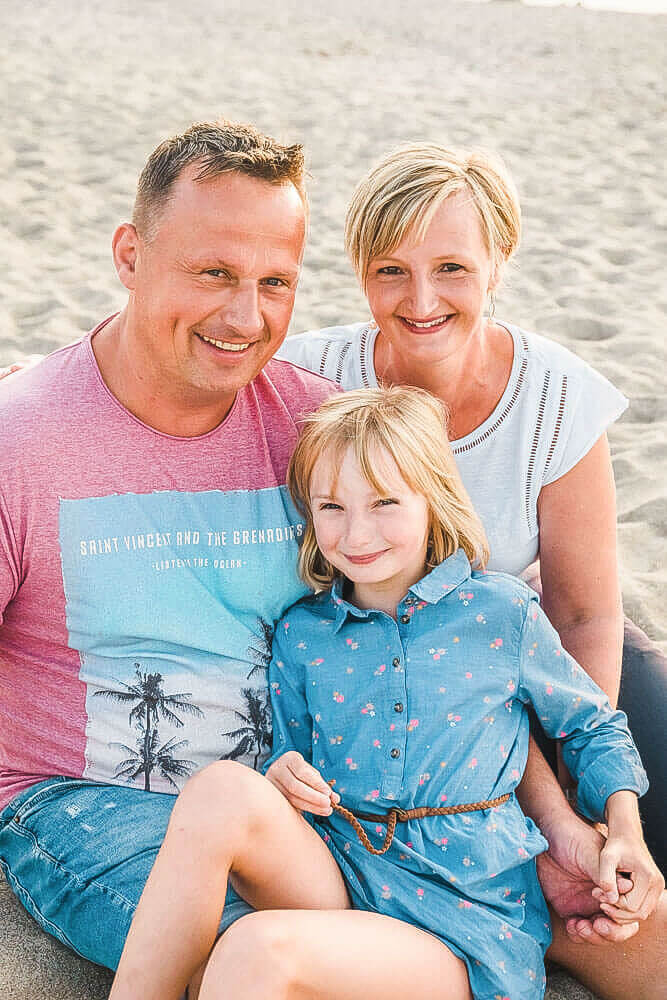 Familien-Fotoshooting mit Fotograf aus Rostock Markgrafenheide. Die Familie sitzt am Strand, kuschelt und schaut in die Kamera.