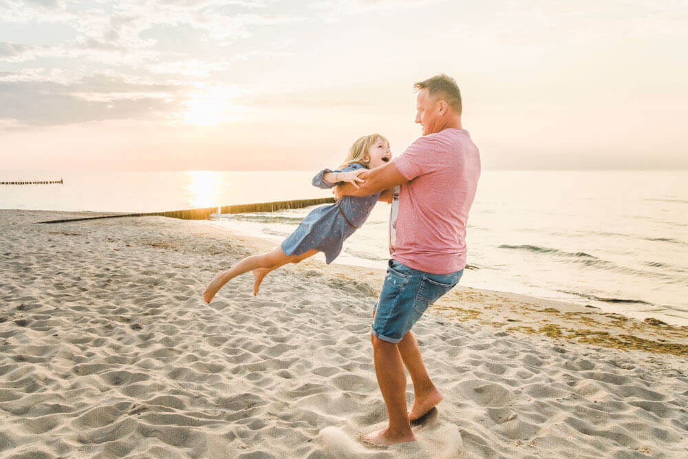 Papa wirbelt seine Tochter durch die Gegend beim Fotoshooting am Strand in Warnemünde zur goldenen Stunde