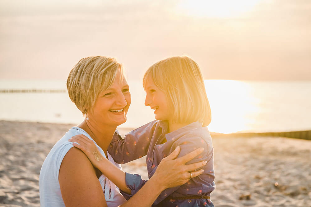 Mama und Tochter lachen sich bei dem Fotoshooting am Strand von Graal-Müritz zum Sonnenuntergang an.