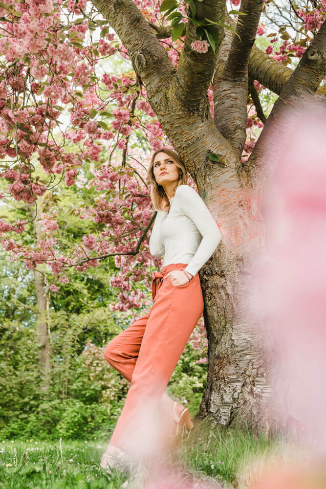 Ganzkörper-Aufnahme von unten von junger Frau und einem Kirschblüten-Baum beim Fotoshooting mit Fotograf aus Rostock im Frühling